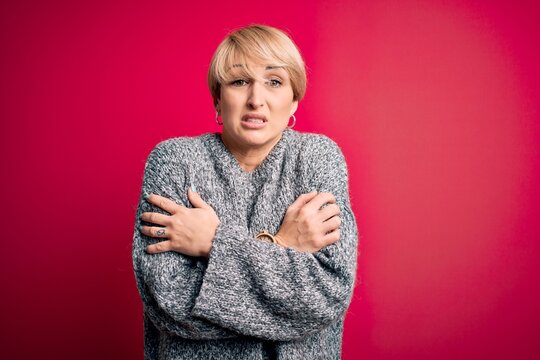 Young blonde woman with modern short hair wearing casual sweater over pink background shaking and freezing for winter cold with sad and shock expression on face