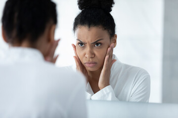 Head shot close up unhappy African American young woman checking skin, touching cheeks, angry girl...