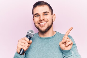 Young handsome man singing song using microphone smiling happy pointing with hand and finger to the side