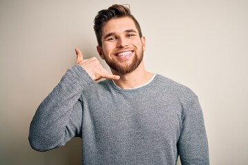 Young handsome blond man with beard and blue eyes wearing casual sweater smiling doing phone gesture with hand and fingers like talking on the telephone. Communicating concepts.