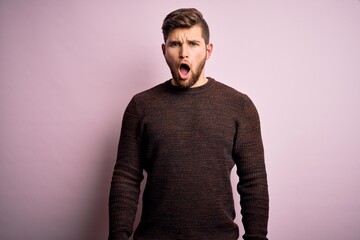 Young blond man with beard and blue eyes wearing casual sweater over pink background In shock face, looking skeptical and sarcastic, surprised with open mouth
