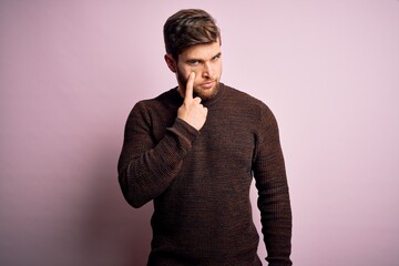 Fototapeta premium Young blond man with beard and blue eyes wearing casual sweater over pink background Pointing to the eye watching you gesture, suspicious expression