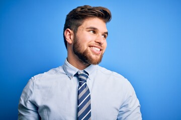 Young blond businessman with beard and blue eyes wearing elegant shirt and tie standing looking away to side with smile on face, natural expression. Laughing confident.