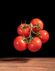 Bouquet of organic red tomatoes falling into a wood table with black background