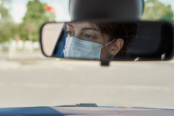 Woman in protective mask driving car, reflection in mirror