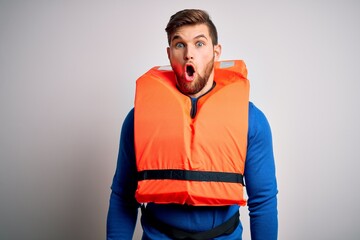 Young blond tourist man with beard and blue eyes wearing lifejacket over white background afraid...