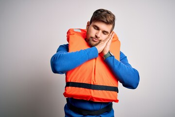 Young blond tourist man with beard and blue eyes wearing lifejacket over white background sleeping...