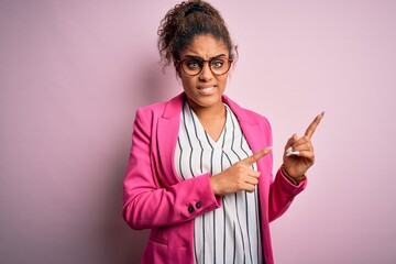Beautiful african american businesswoman wearing jacket and glasses over pink background Pointing aside worried and nervous with both hands, concerned and surprised expression