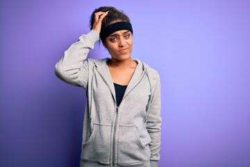 Fototapeta na wymiar Young african american sportswoman doing sport wearing sportswear over purple background confuse and wonder about question. Uncertain with doubt, thinking with hand on head. Pensive concept.