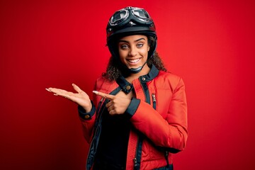Young african american motorcyclist girl wearing moto helmet and glasses over red background amazed...