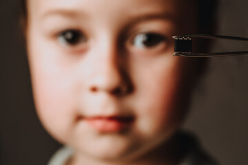 A tweezers holds a black microchip on the background of the face.