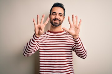Fototapeta premium Young handsome man with beard wearing casual striped t-shirt standing over white background showing and pointing up with fingers number nine while smiling confident and happy.