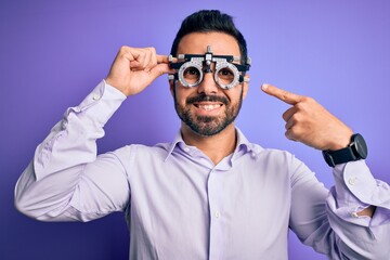 Young handsome optical man with beard wearing optometry glasses over purple background very happy pointing with hand and finger