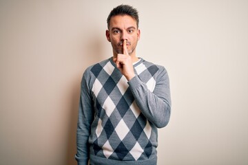 Obraz premium Young handsome man wearing casual sweater standing over isolated white background asking to be quiet with finger on lips. Silence and secret concept.