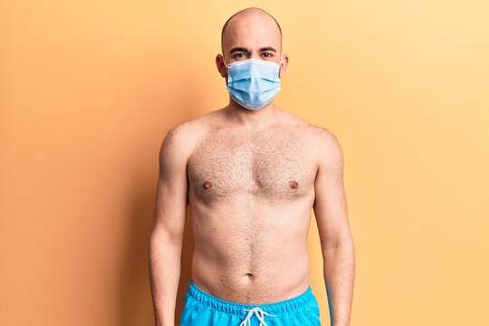 Young handsome bald man shirtless wearing swimwear and medical mask with a happy and cool smile on face. lucky person.