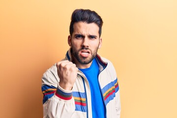 Young handsome man with beard wearing casual jacket angry and mad raising fist frustrated and furious while shouting with anger. rage and aggressive concept.