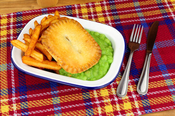 Steak and kidney pie and chips meal with mushy peas in a metal enamel dish