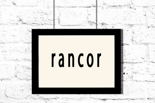 Black frame hanging on white brick wall with inscription rancor