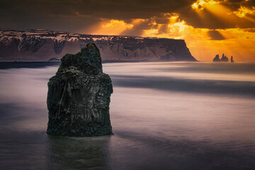 Sunset over coastal volcanic rocks and cliffs at Reynisfjara black sand beach in Iceland