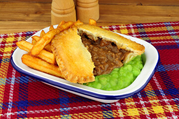 Steak and kidney pie and chips meal with mushy peas in a metal enamel dish