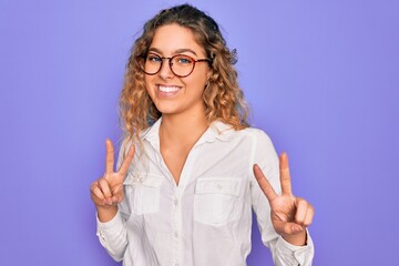 Young beautiful woman with blue eyes wearing casual shirt and glasses over purple background smiling looking to the camera showing fingers doing victory sign. Number two.