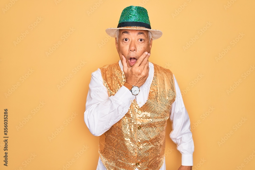 Poster Middle age senior grey-haired man wearing Brazilian carnival custome over yellow background Looking fascinated with disbelief, surprise and amazed expression with hands on chin