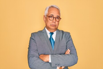Middle age senior grey-haired handsome business man wearing glasses over yellow background skeptic and nervous, disapproving expression on face with crossed arms. Negative person.