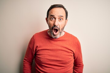 Middle age hoary man wearing casual orange sweater standing over isolated white background afraid and shocked with surprise and amazed expression, fear and excited face.