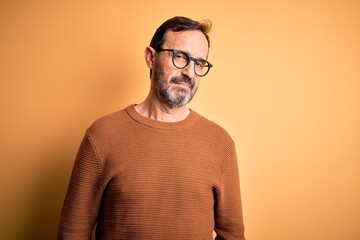 Middle age hoary man wearing brown sweater and glasses over isolated yellow background looking sleepy and tired, exhausted for fatigue and hangover, lazy eyes in the morning.