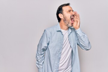 Middle age handsome man wearing casual denim shirt standing over isolated white background shouting and screaming loud to side with hand on mouth. Communication concept.