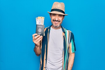 Middle age tourist man on vacation holding united states passport with boarding pass looking positive and happy standing and smiling with a confident smile showing teeth