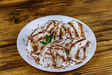 Vanilla ice cream with chocolate topping in white plate on a wooden table