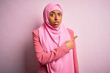 Young African American afro woman wearing muslim hijab over isolated pink background Pointing aside worried and nervous with forefinger, concerned and surprised expression
