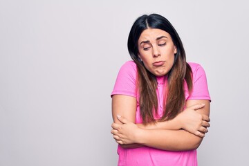 Obraz premium Young beautiful brunette woman wearing casual pink t-shirt standing over white background shaking and freezing for winter cold with sad and shock expression on face