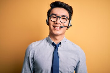 Young handsome chinese call center agent man wering glasses using headset with a happy and cool...