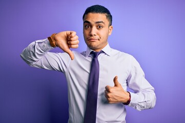 Young brazilian businessman wearing elegant tie standing over isolated purple background Doing thumbs up and down, disagreement and agreement expression. Crazy conflict