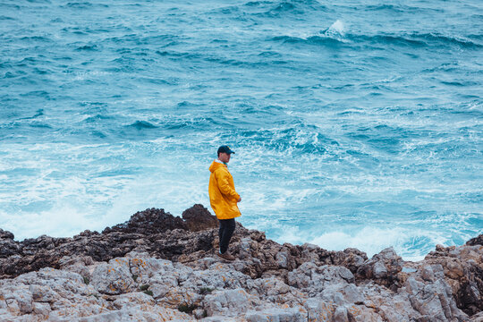 man walking by rock to storming sea