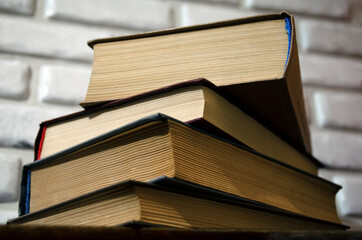 A stack of old books on a table against a white brick wall.