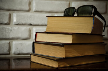 A stack of old books and glasses on a table against a white brick wall.