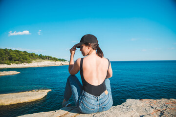 young pretty woman sitting on the cliff looking at sea