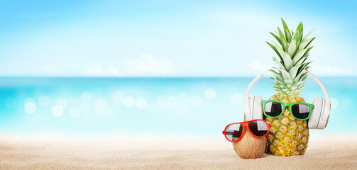 Pineapple with sunglasses and headphones on hot sand beach