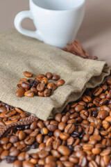 Roasted coffee beans, a white Cup, and a small burlap bag in close-up. Roasted coffee beans of the morning mood.
