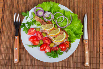 Baked ocean perch on dish, knife, fork on table mat