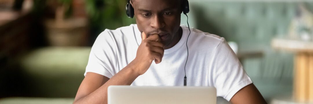 Focused African student wear headphones studying on-line do exercise using laptop, watching video, learning language, self-education, e-study concept. Horizontal photo banner for website header design