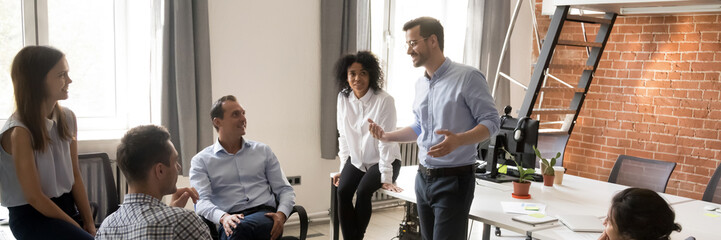 Multi ethnic corporate staff listen team leader company boss during morning briefing in coworking...