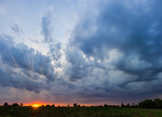 Sky with clouds and sun over the field at sunset