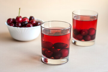 Homemade compote juice with cherries in a transparent glass on a beige background. Fresh summer drink