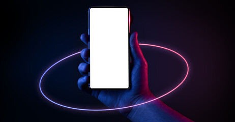 Phone in hand. Silhouette of male hand holding bezel-less smartphone with futuristic neon light circle on dark background. Screen is cut with clipping path. - 356050637