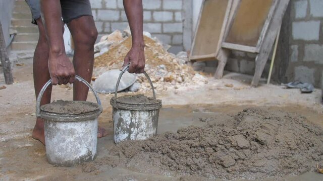 local guy gathers grey wet cement into basket on construction territory slow motion close view. Concept slavery and poverty