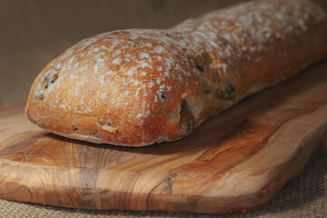 Fresh sourdough bread with olives and dried tomato on a wooden board and hessian table cloth.